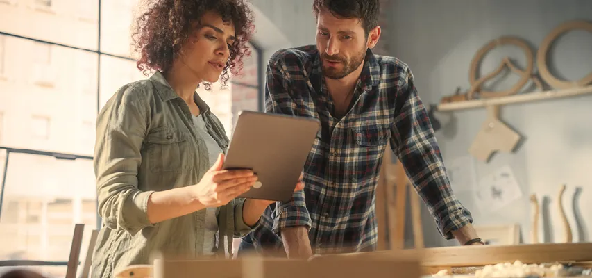 Zwei Handwerker in der Werkstatt bei der Planung nachhaltiger Möbel mit einem Tablet, Symbol für moderne Fertigung, Qualität und verantwortungsbewusste Produktion.